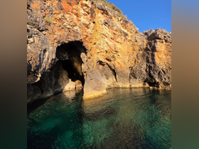 A stunning view of a rocky cave along the coastline, with crystal-clear waters reflecting the vibrant colors of the rocks — perfect for exploring natural wonders on a boating adventure.