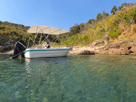 A small boat anchored near a rocky beach, with a person enjoying the sun and water — a perfect spot for relaxation and adventure.