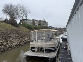 A pontoon boat is docked along a rocky shoreline, showcasing its spacious design and comfortable seating, perfect for leisurely outings on the water.