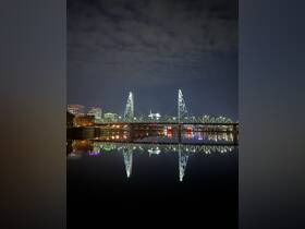 A nighttime view of a bridge reflecting in the water, showcasing the city skyline and illuminated structures.