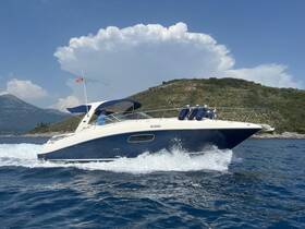A sleek speedboat navigates through clear waters, showcasing its elegant design and performance against a scenic backdrop of hills and clouds.