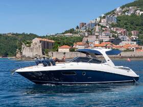 A sleek boat cruises through clear waters with a scenic backdrop of coastal buildings and greenery, perfect for summer adventures on the water.
