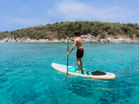 A paddleboarder enjoys the clear turquoise waters, surrounded by scenic coastal views — a perfect snapshot of adventure on the water.