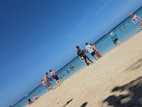 A lively beach scene with groups of people enjoying the sun and swimming in clear waters, perfect for a fun day out on vacation.