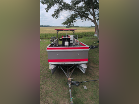 A rear view of a colorful boat parked on grass, showcasing its structure and design against a rural backdrop.