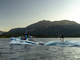 A thrilling wakeboarding session on a beautiful lake, with friends enjoying the ride aboard a stylish boat against a stunning mountain backdrop.