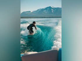 A surfer skillfully rides a wave in crystal-clear waters, with stunning mountain scenery in the background — an exhilarating moment on the water.
