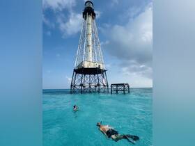 Two snorkelers explore the vibrant waters near a historic lighthouse, showcasing the beauty of underwater adventures in a tropical paradise.