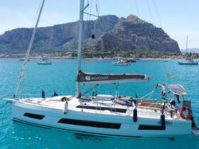 A stunning Dufour yacht anchored in crystal-clear turquoise waters, with a picturesque backdrop of cliffs and a charming coastal town.