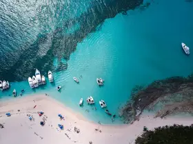 A stunning aerial view of a beach with multiple boats anchored in turquoise waters, showcasing a vibrant scene of relaxation and fun under the sun.