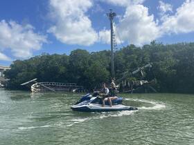 A couple enjoys a thrilling ride on a jet ski, exploring the mangroves and an abandoned boat in the background — a perfect adventure for water enthusiasts.