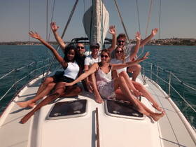 A joyful group of friends poses on the deck of a sailboat, celebrating their sailing adventure on clear blue waters.