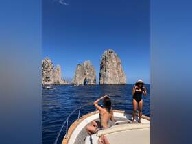 Two friends enjoy a sunny day on a boat near the iconic Faraglioni rocks in Capri, capturing the perfect moment against a stunning backdrop.