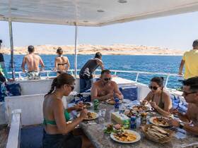 A lively group enjoys a delicious meal aboard a boat, surrounded by stunning ocean views — perfect for social dining experiences on the water.