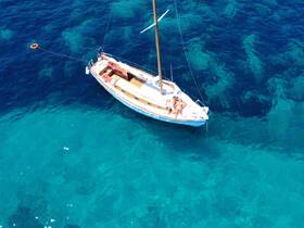 Aerial view of a sailboat with guests relaxing on deck in crystal-clear waters, perfect for a day of sun and sailing adventures.