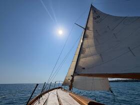 A stunning view of a sailboat in motion, showcasing its sails against a clear blue sky and sunlit ocean — perfect for sailing enthusiasts and adventure seekers.