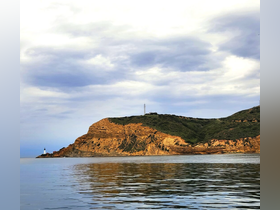 A stunning view of a rugged coastline with a lighthouse, reflecting beautifully in the calm waters — an ideal backdrop for boating adventures.