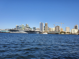 A stunning view of a large naval ship docked alongside a vibrant city skyline, showcasing the blend of maritime and urban landscapes.