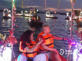 A couple enjoys a festive boat ride illuminated by colorful lights during a beautiful evening, capturing the essence of a memorable night on the water.