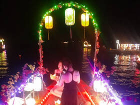 Two friends enjoy a festive night on a beautifully decorated boat, surrounded by colorful lanterns and shimmering water — perfect for memorable celebrations.