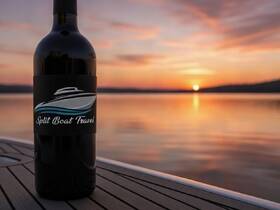 A bottle of wine with a boat logo sits on a dock at sunset, creating a serene atmosphere perfect for evening boat trips.