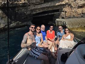 A cheerful group of friends poses for a photo on a boat near a stunning cave, capturing the essence of adventure and camaraderie on the water.