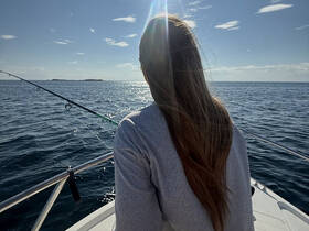 A woman enjoys a peaceful fishing experience on a boat, surrounded by sparkling ocean waters under a bright sky.