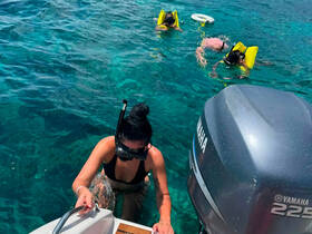 A group enjoys snorkeling in crystal-clear waters, with one person climbing back onto the boat while others explore underwater — a perfect adventure for water enthusiasts.
