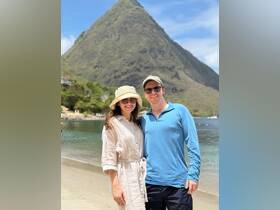 A happy couple poses for a photo on the beach with a stunning mountain backdrop, capturing a memorable moment during their tropical getaway.