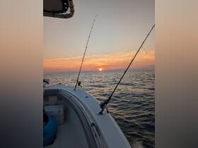 A serene sunset view from a fishing boat, with fishing rods in the foreground, capturing the essence of a peaceful evening on the water.