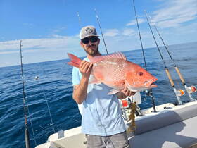 A proud angler holds up a large snapper while fishing on a boat, showcasing the thrill of deep-sea fishing adventures.