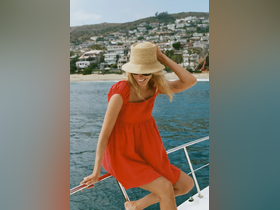 A joyful woman enjoys a sunny day on a boat, showcasing the perfect summer vibe against a beautiful coastal backdrop.