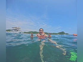 A joyful swimmer gives a peace sign while enjoying the clear ocean waters, with a catamaran in the background — a perfect snapshot of a fun day on the water.