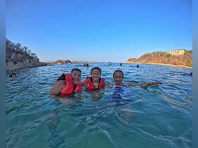 A joyful group enjoys a refreshing swim in clear waters, showcasing the fun and excitement of a beach day with life jackets for safety.