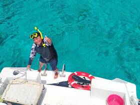 A snorkeler gives a thumbs up while climbing aboard a boat, showcasing the vibrant turquoise waters — perfect for underwater adventures.