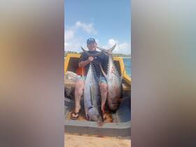 A proud angler displays his impressive catch of two large fish while sitting in a boat, showcasing the thrill of a successful fishing trip.