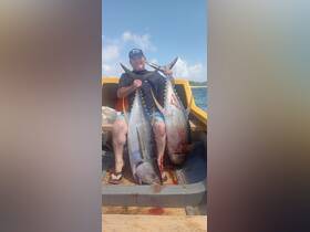 A proud angler displays his impressive catch of two large tuna aboard a fishing boat, showcasing the thrill of deep-sea fishing adventures.