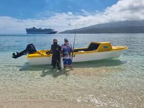 Two anglers proudly display their catch while standing in shallow water next to their boat, with a cruise ship in the background — a perfect day of fishing in paradise.