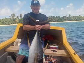 A proud angler displays his impressive catch of a tuna while aboard a boat, showcasing the thrill of fishing in beautiful ocean waters.