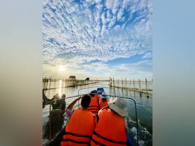 A group of passengers in orange life jackets enjoy a scenic boat ride at sunset, navigating through tranquil waters surrounded by fishing nets — a perfect experience for nature lovers.