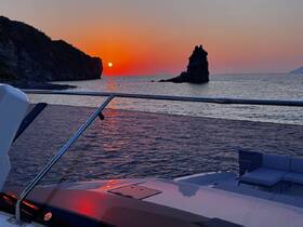 A stunning sunset view from the deck of a boat, showcasing the tranquil waters and rocky coastline — perfect for romantic evening cruises.