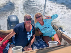 Two friends enjoy a fun day on the water, capturing the joy of boating with smiles and peace signs as they cruise along.
