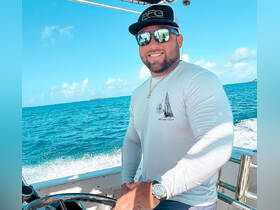 A smiling captain navigates the boat through beautiful turquoise waters, showcasing the joy of a day on the ocean.