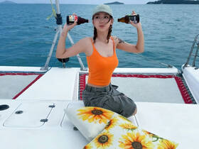 A joyful moment on a catamaran as a young woman playfully poses with drinks, capturing the essence of fun and relaxation on the water.