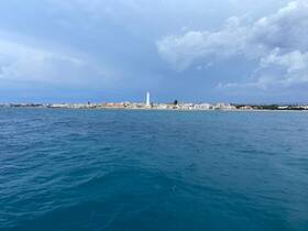A picturesque view of the coastline featuring a lighthouse and colorful buildings, showcasing the beauty of the destination from the water.