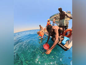 A lively group enjoys a snorkeling experience, interacting with fish from the side of their boat — perfect for family adventures on the water.