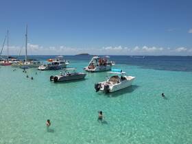 A vibrant scene at a sandbar with multiple boats anchored and guests enjoying the clear waters — perfect for a fun day of swimming and relaxation.