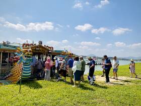 A lively group gathers around a colorful dragon boat, ready for an exciting water tour. The vibrant decorations and scenic backdrop enhance the festive atmosphere.