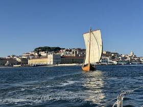 A traditional sailboat glides through the waters near a vibrant cityscape, showcasing the beauty of maritime exploration against a picturesque backdrop.