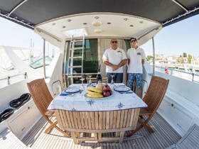 Two crew members stand in the dining area of a yacht, showcasing a beautifully set table with fresh fruits, perfect for onboard dining experiences.